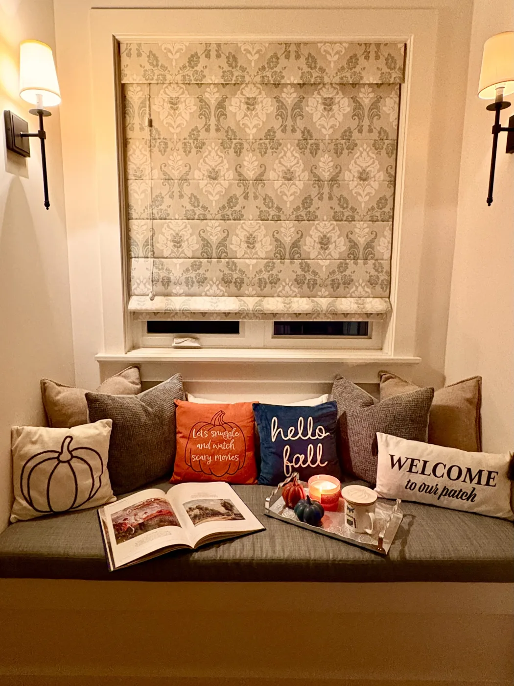 Cozy fall window seat with seasonal pillows beneath a patterned Roman shade