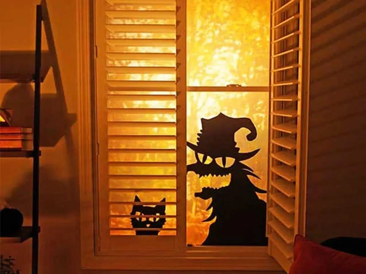 Plantation shutters with spooky black cat and witch silhouettes glowing in a Halloween window
